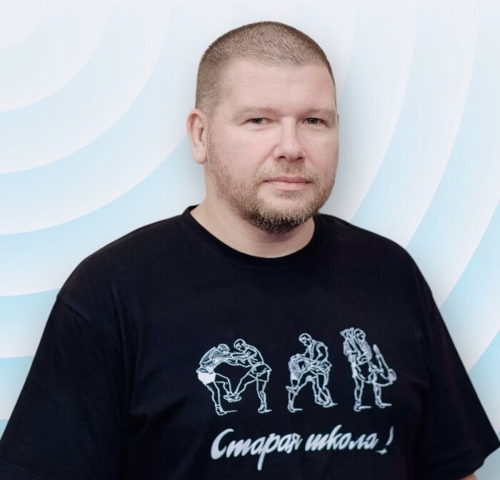 Андрей Абашин, главный тренер клуба «Схватка», мастер спорта России по самбо — портрет в чёрной футболке на светло-голубом фоне
