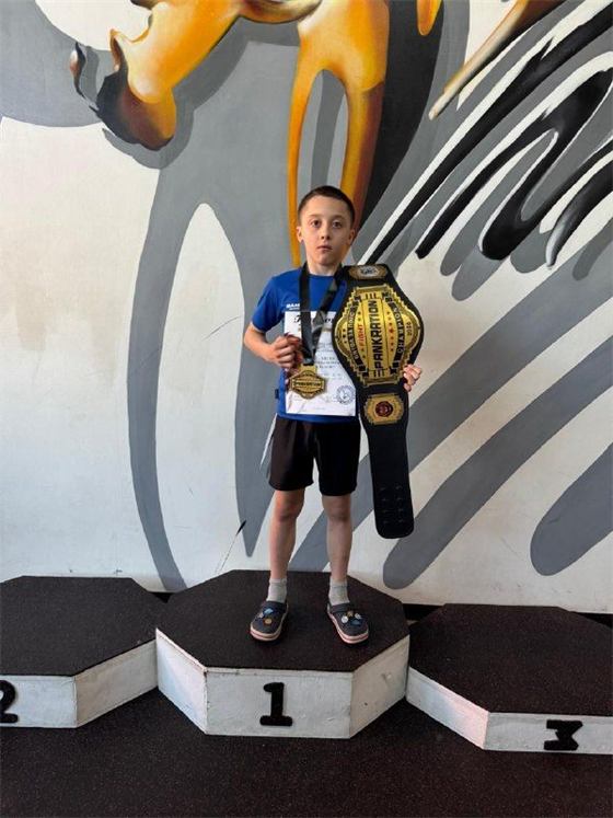 Мальчик в синей футболке с чемпионским поясом по панкратиону на первой ступени пьедестала