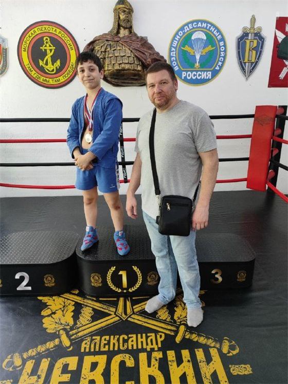 Мальчик в синей самбовке с медалью на первой ступени пьедестала турнира «Александр Невский»